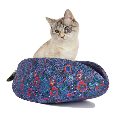 The Cat Canoe® taco-shaped modern cat bed, is made here in a festive floral print with shades of blue and bright accents or coral pink. The cat model weighs about 7 pounds, the bed fits pets to about 18 pounds. 