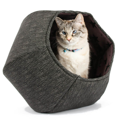 The Cat Ball® cat bed is a hexagonal cat bed with two openings, made with a tonal black wood grain print cotton fabric, and lined with black stars on a purple background. This pet bed is made in the USA.